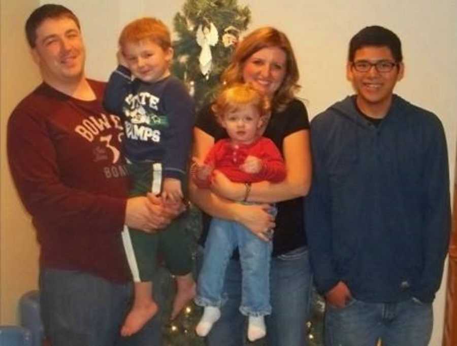 Family with teen foster son and two young biological sons take a family photo in front of their Christmas tree