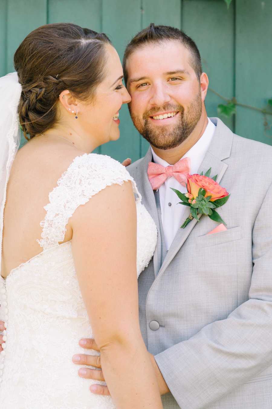 Woman smiles at her husband while he smiles at the camera during wedding photoshoot