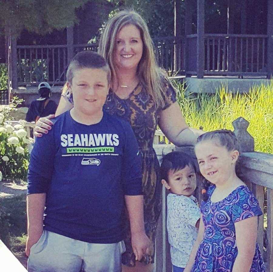 Mother who had miscarriage with fourth child stands smiling with three children 