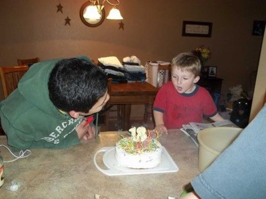 Foster son blows out the candles on his 18th birthday cake while wearing a green hoodie