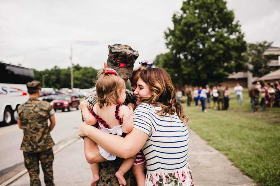 Soldier father who just returned home holds two daughter and wife wraps her arms around them all