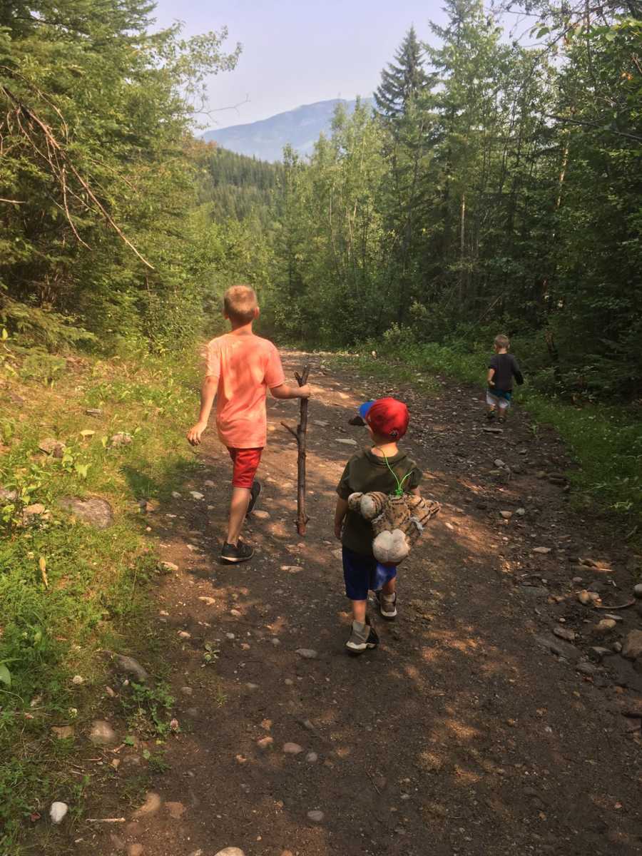 Young boy who has connection with animals walks trail with big stick with two younger boys