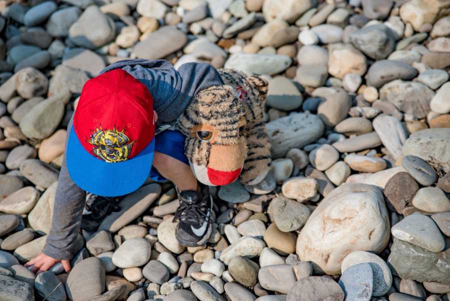 Toddler sitting on pile of rocks with stuffed animal tiger