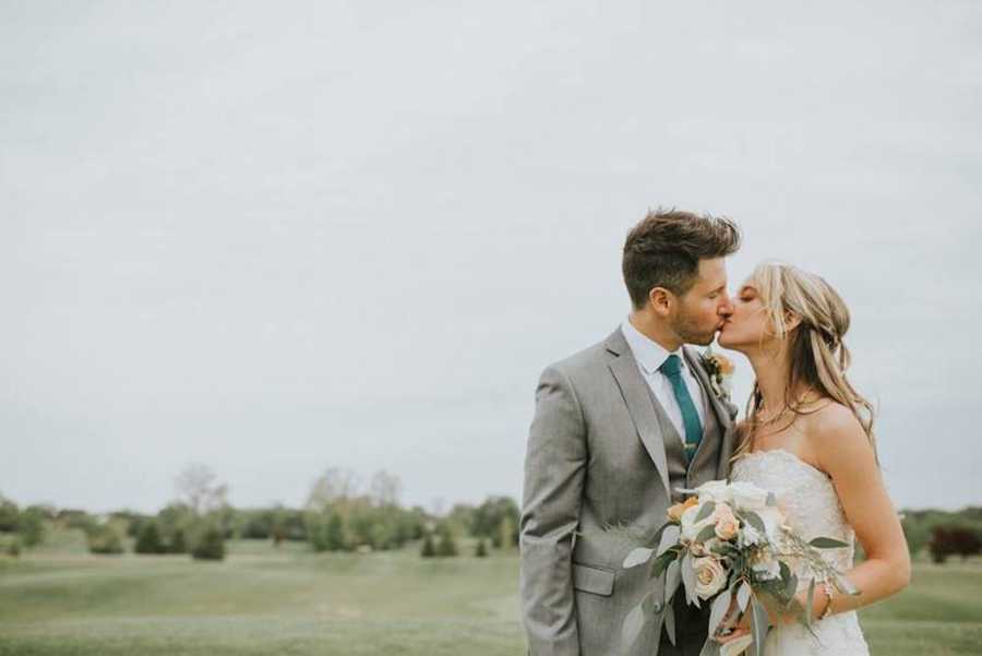 Bride with crohn's disease kisses groom outside holding bouquet of flowers