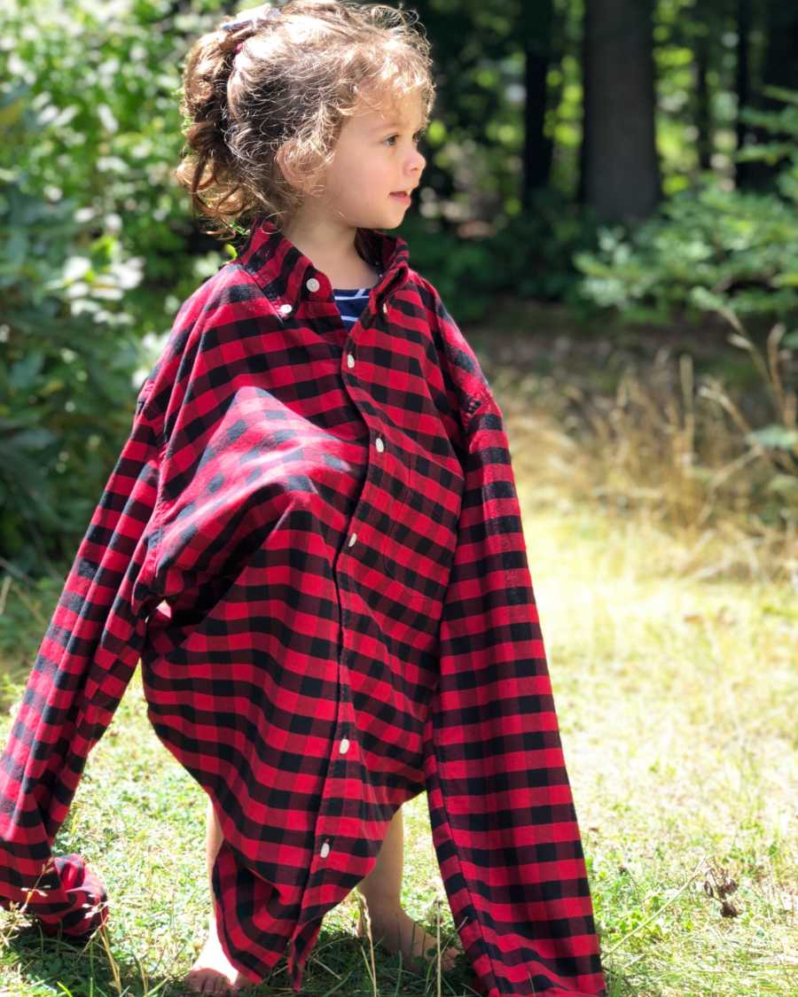 Toddler standing in grass wearing flannel shirt her father wore when she was born
