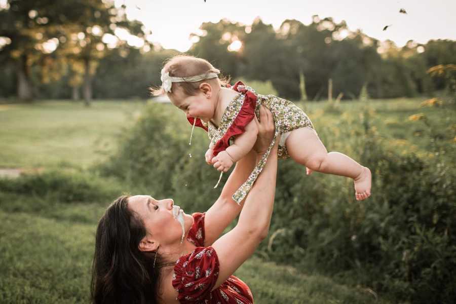 Mother holding baby in the air who is spitting up at her