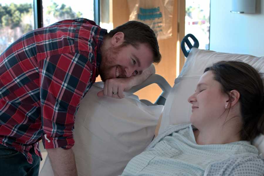 Husband who tended to pregnant wife's every need rests his head on hospital bed where his wife lays