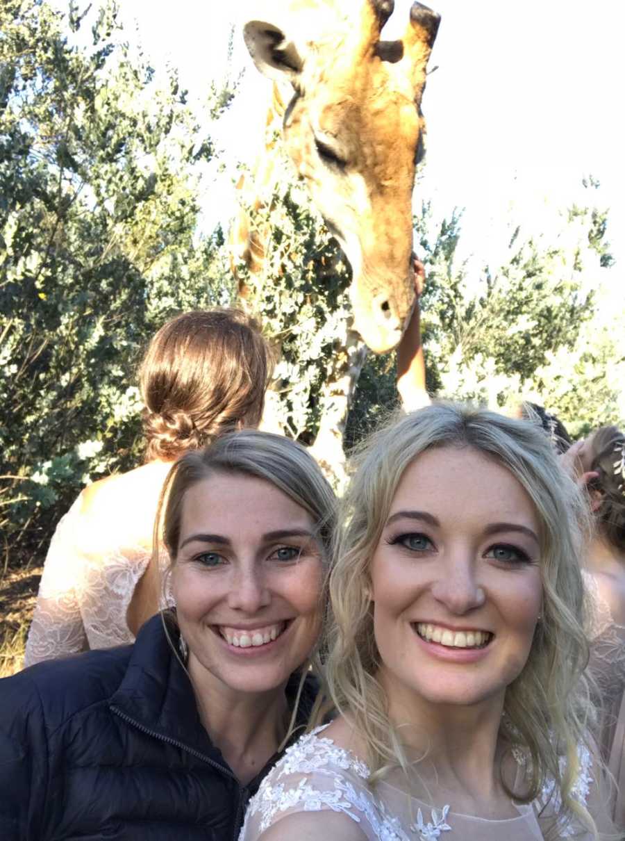 Bride smiles with woman in selfie with giraffe in background