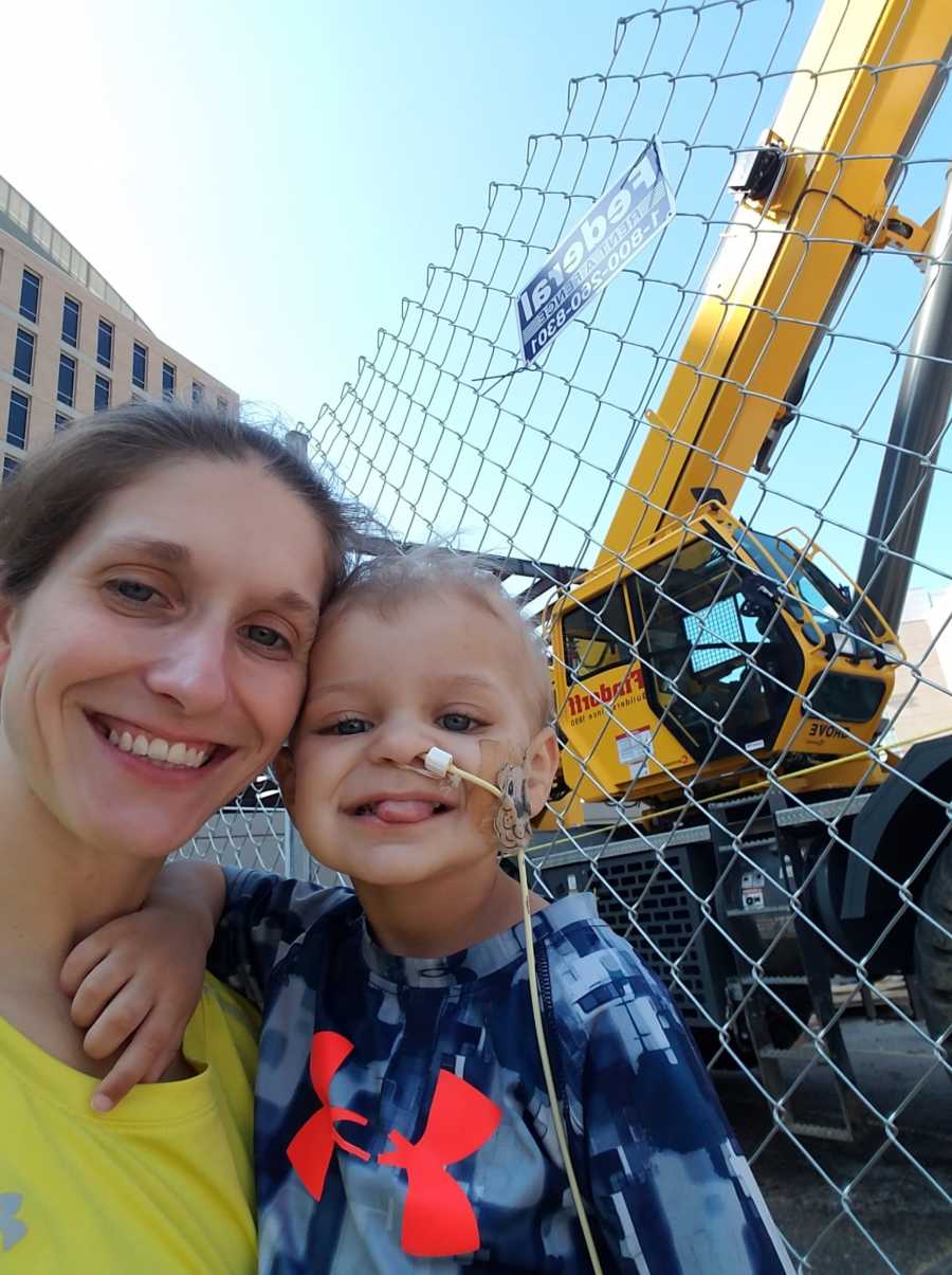 Mother smiles in selfie with son who has cancer beside construction site that fascinates him