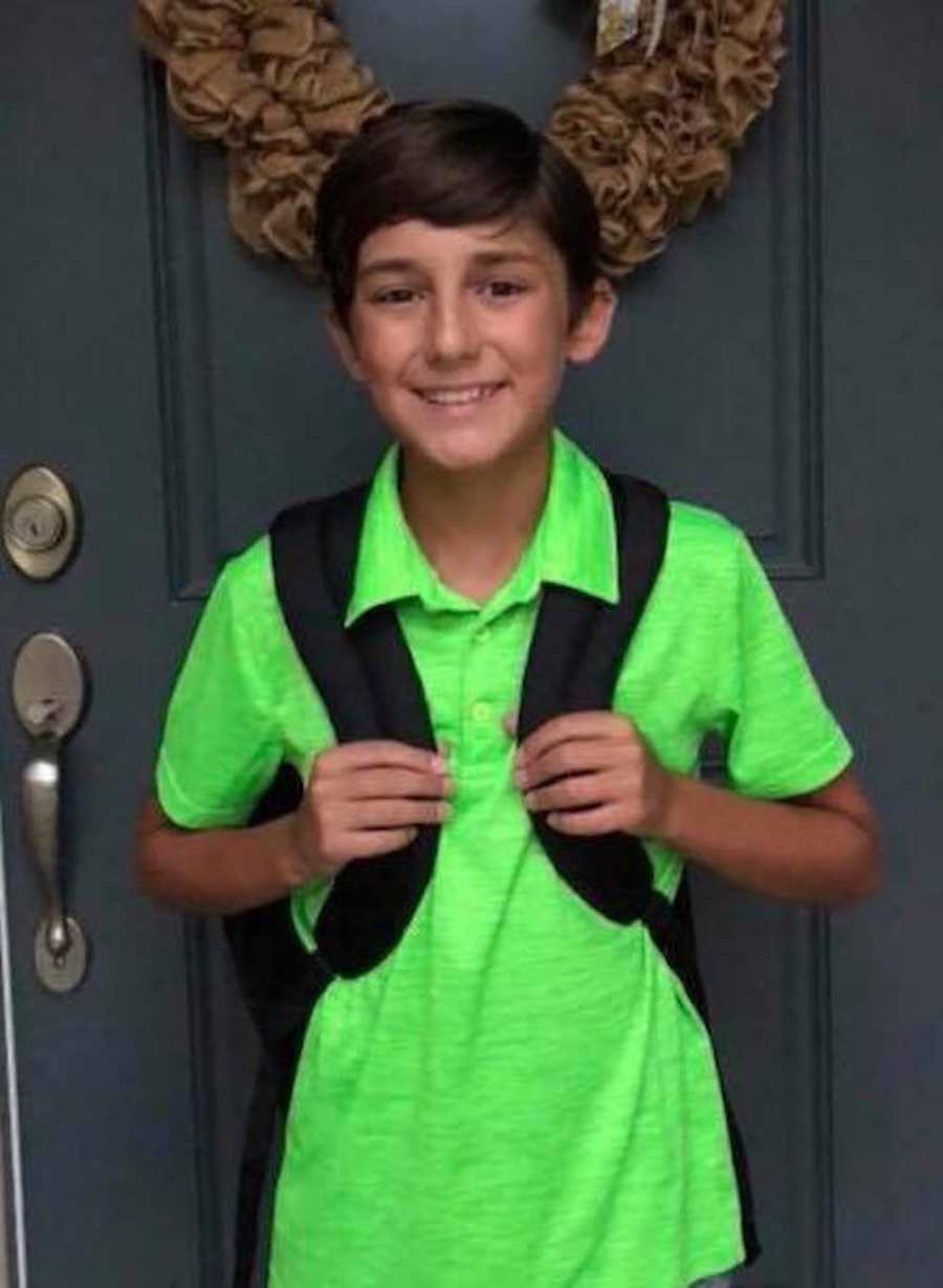 Young boy wearing green shirt smiles in front of front door on school picture day 