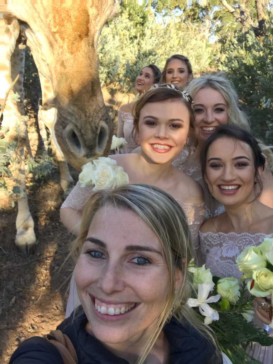 Woman takes selfie with bridal party with giraffe right next to them at wedding on South African reserve