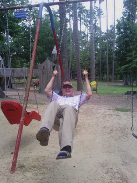 Elderly man smiles while swinging on swing set