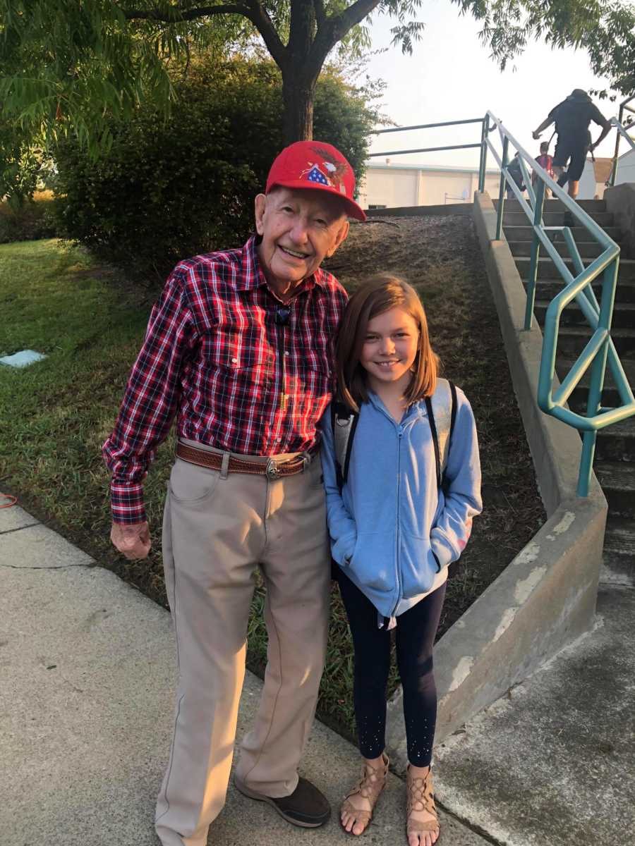 Old man who stands outside middle school to encourage kids stands smiling with arm around young girl