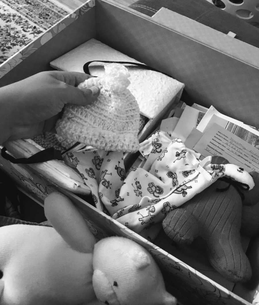 Woman who had stillborn holds baby hat next to box full of things meant for the baby