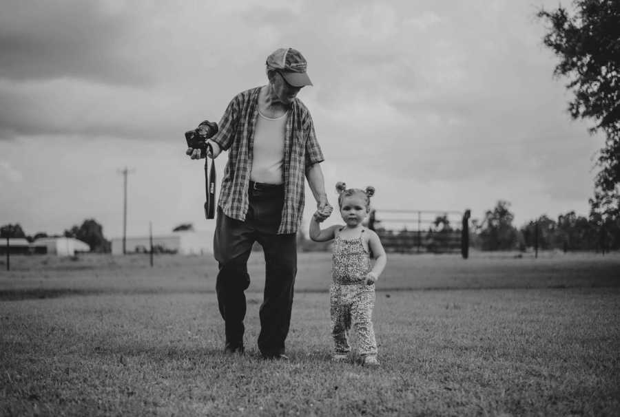 Elderly man walking hand in hand with young granddaughter while his other hand holds camera