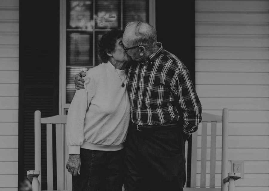 Elderly husband and wife with dialysis kiss outside of their home