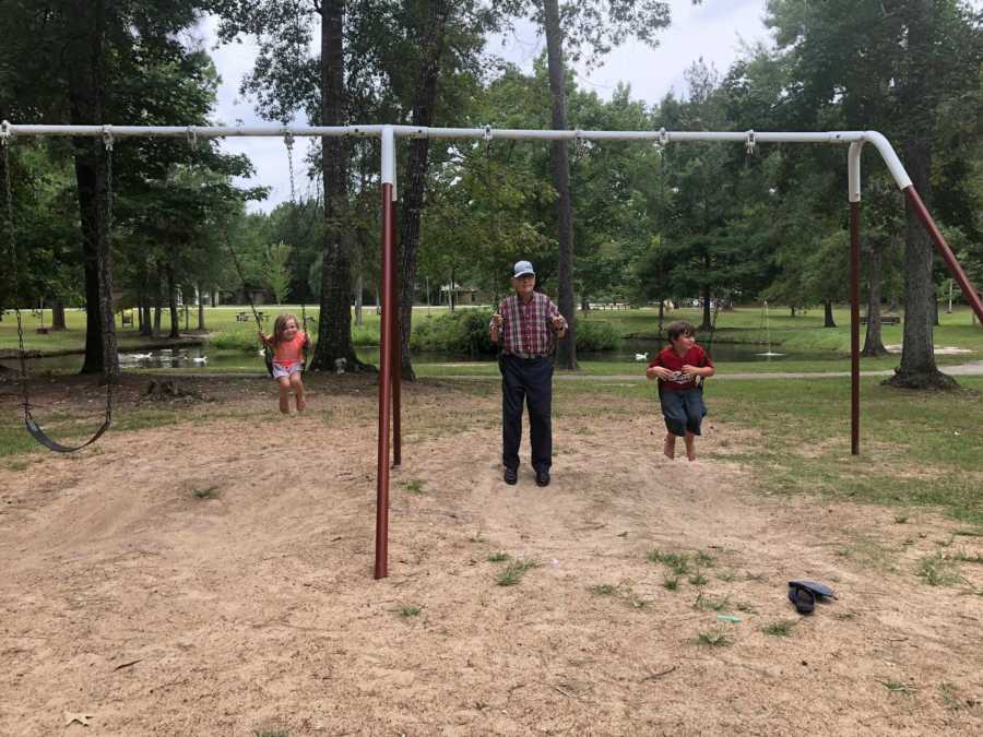 Grandfather sits on swing beside his two grandchildren