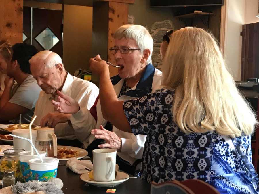 Woman sitting at restaurant table feeding mother with dementia