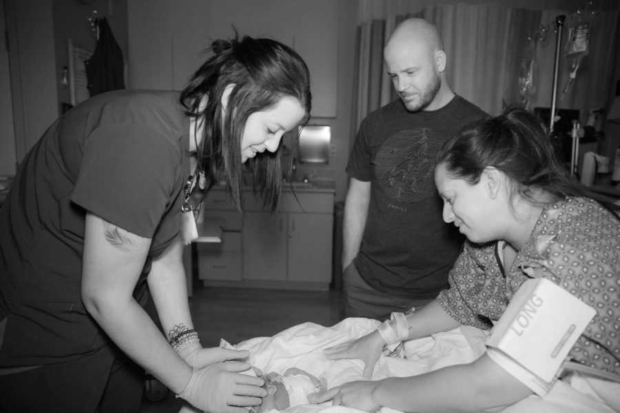 Nurse stands over newborn beside mother and father