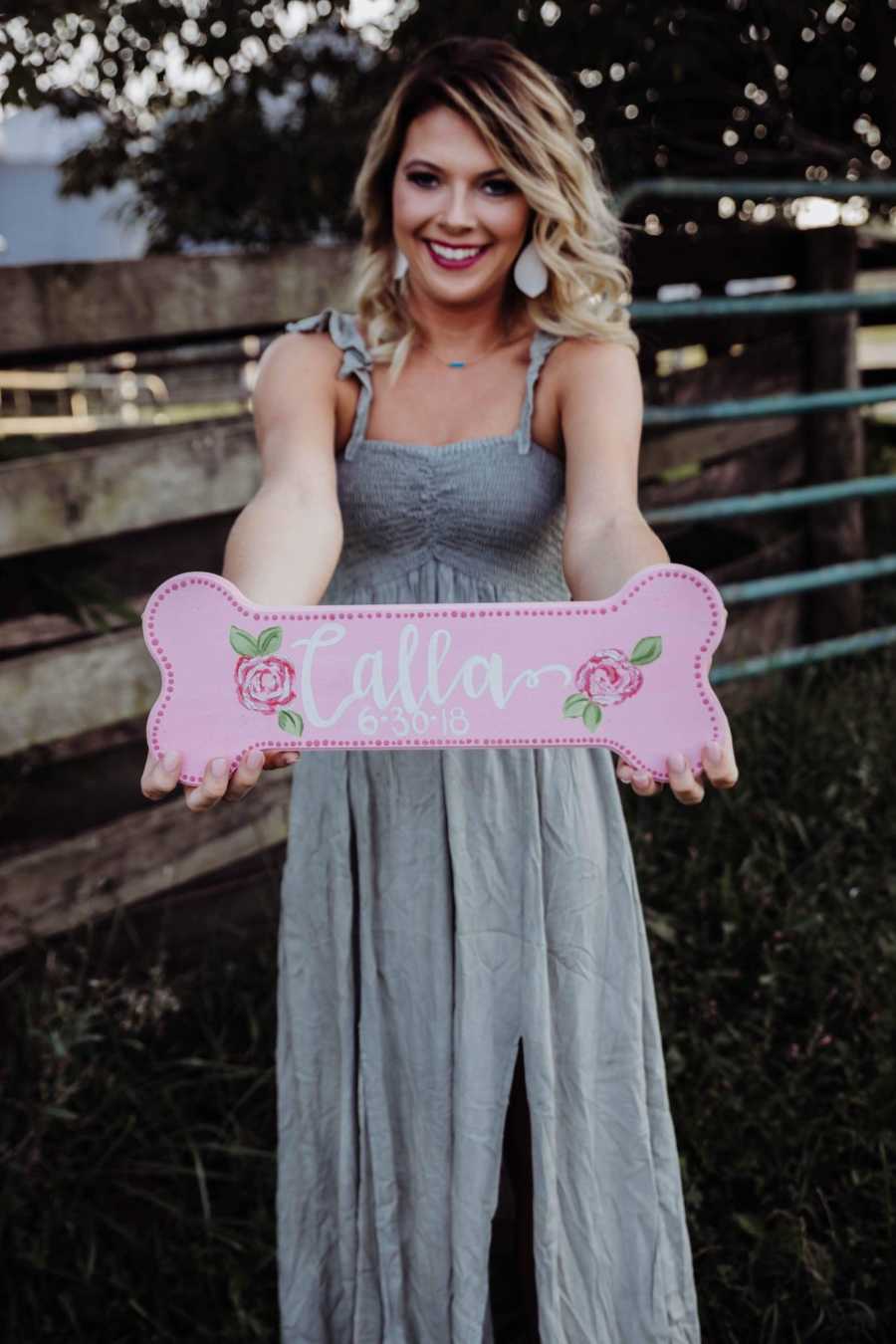 Recently single young woman holds out pink dog bone sign that says, "Calla"