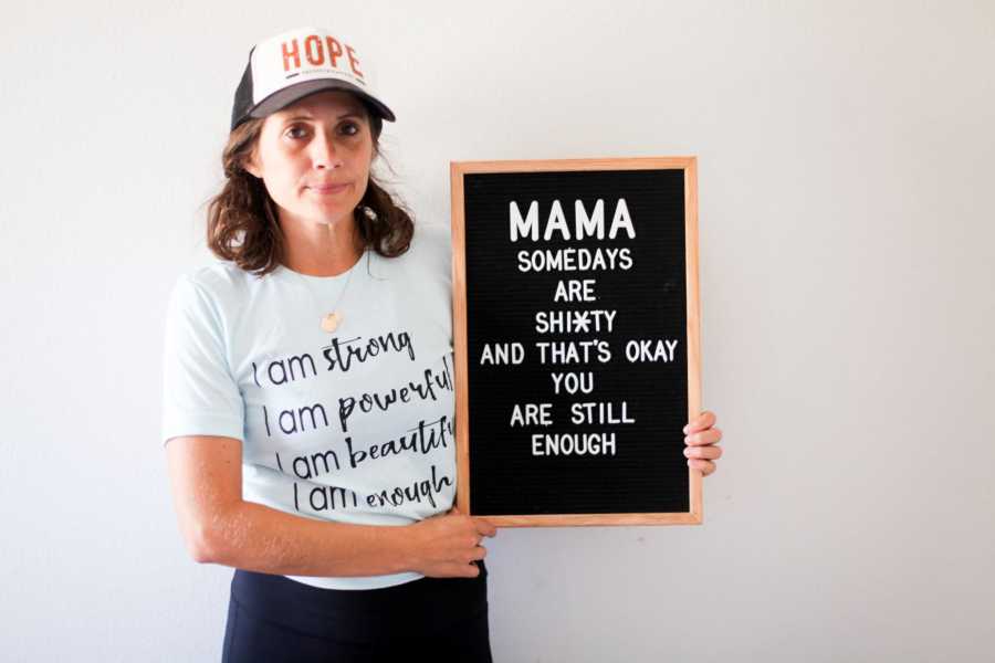 Mother who was overwhelmed when husband went back to work holding sign that says, "Mama some days are shitty"