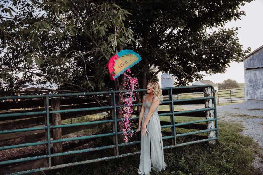 Recently single dog mom stands near recently hit pinata that is releasing pink confetti