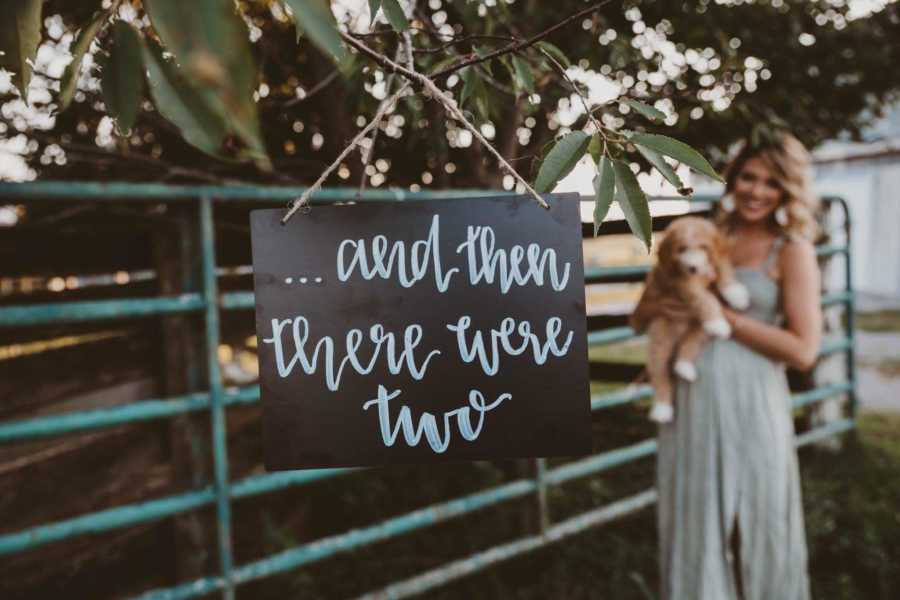 Recently single dog mom holding puppy behind sign that says, "and then there were two"