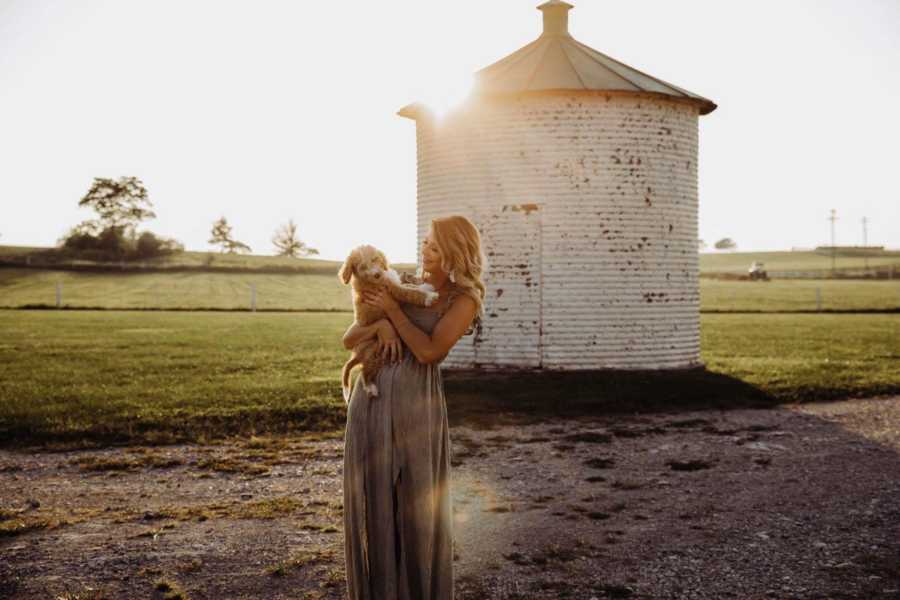 Recently single dog mom holds puppy in front of silo