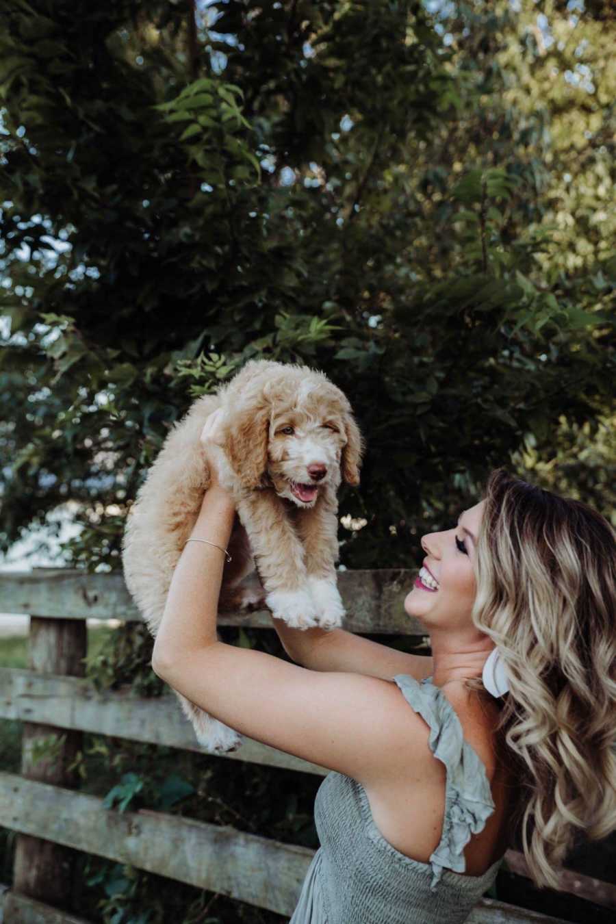 Recently single dog mom smiles as she holds puppy in air