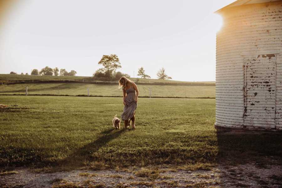 Recently single dog mom walks with puppy beside her next to silo