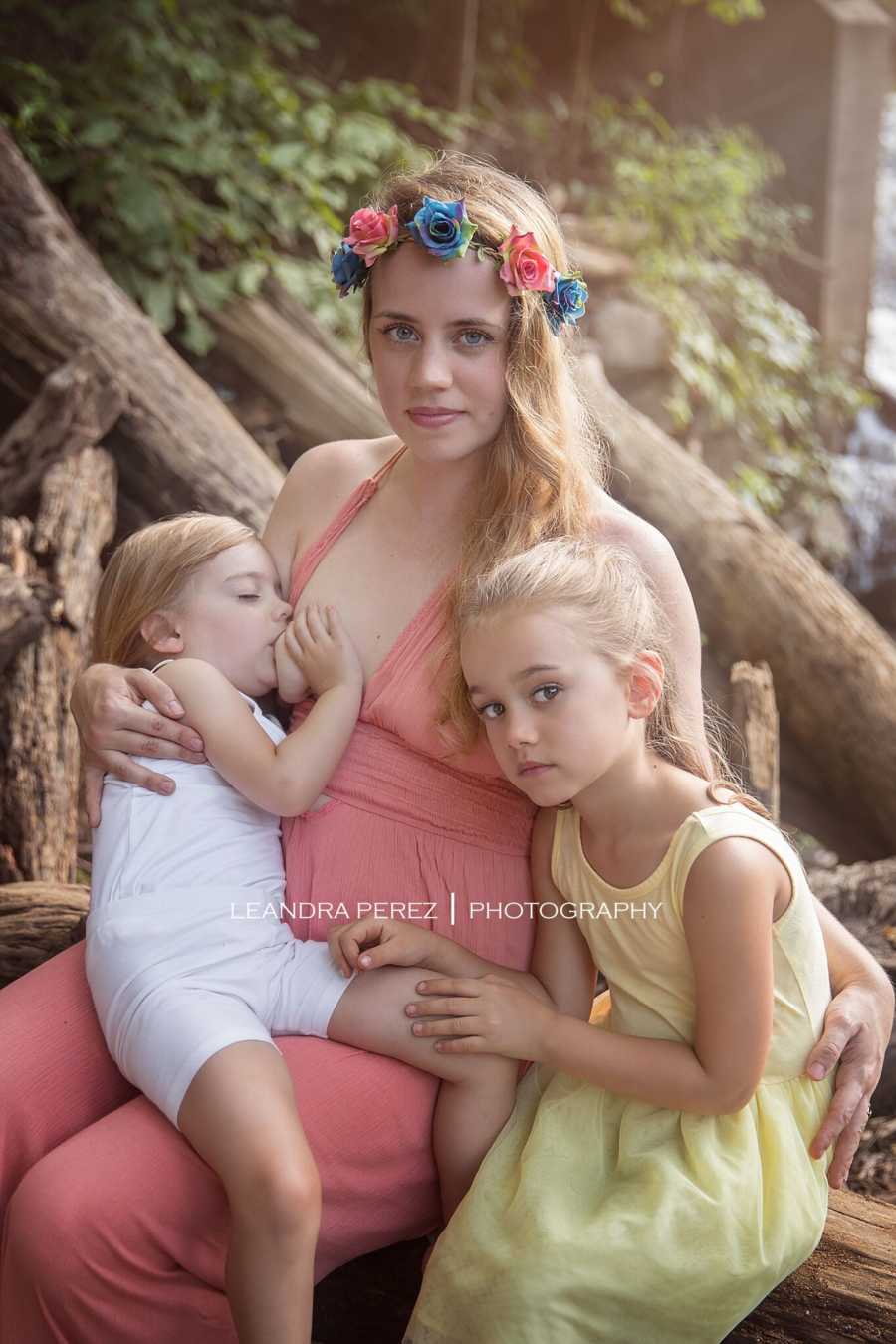 Woman sits breastfeeding three year old daughter beside older daughter
