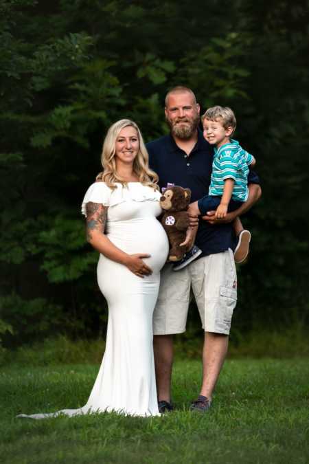 Pregnant woman who suffered child loss stands holding stomach with husband and first born