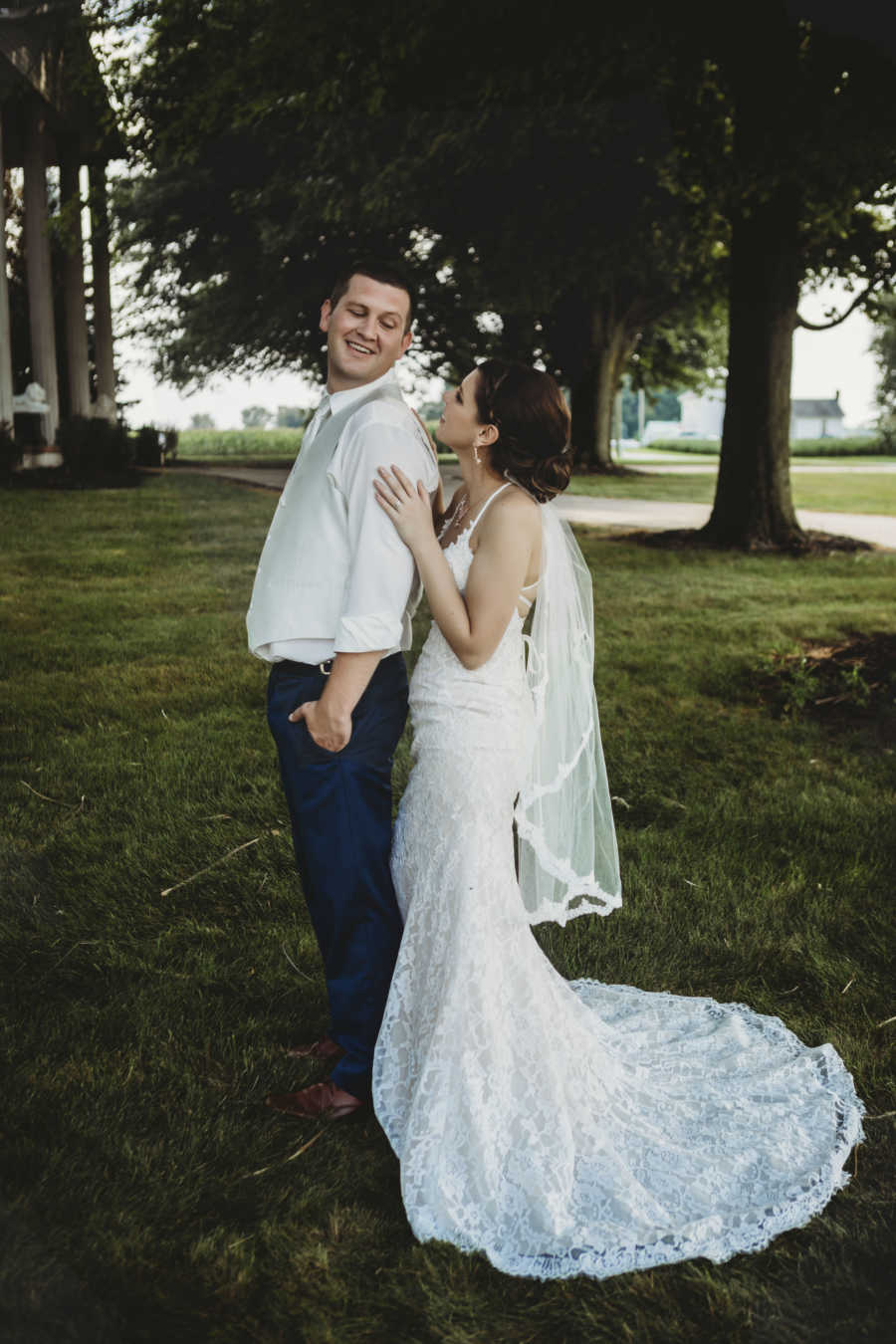 Groom stands with back to wife looking at her over his shoulder as she holds him