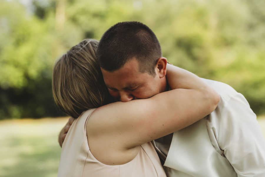 Mother with breast cancer holds oldest son as he cries into her shoulder at wedding