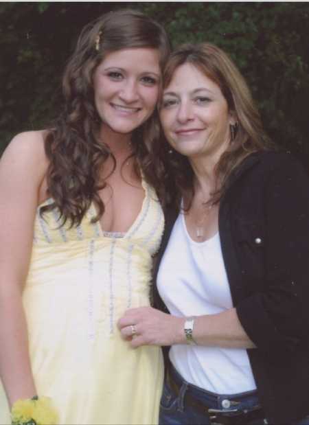 Mom and daughter take a photo together while the daughter is dressed in a yellow dress for prom