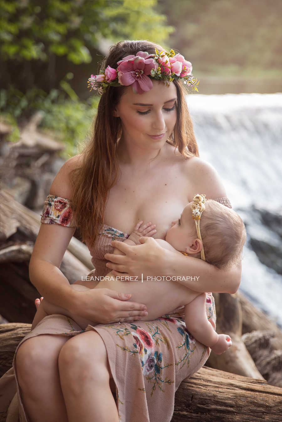 Mother sits beside river breastfeeding