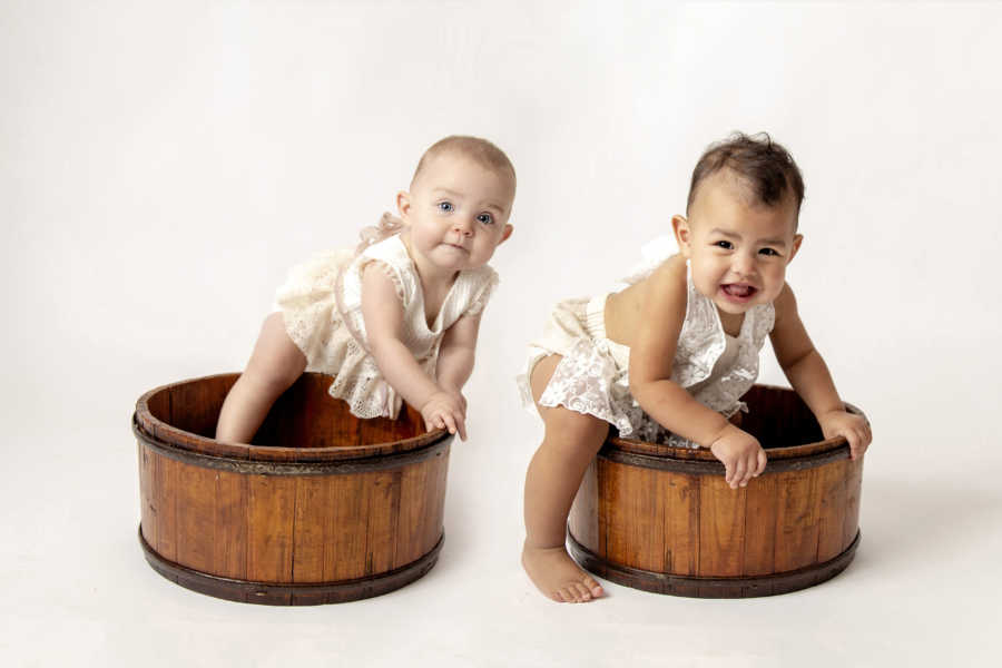 Adopted infant and sister stand in wooden barrels in photoshoot