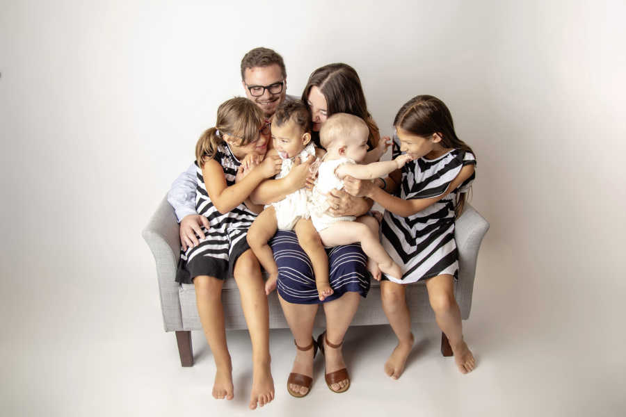 Husband and wife sit on couch with their twin girls, infant daughter, and adopted infant 