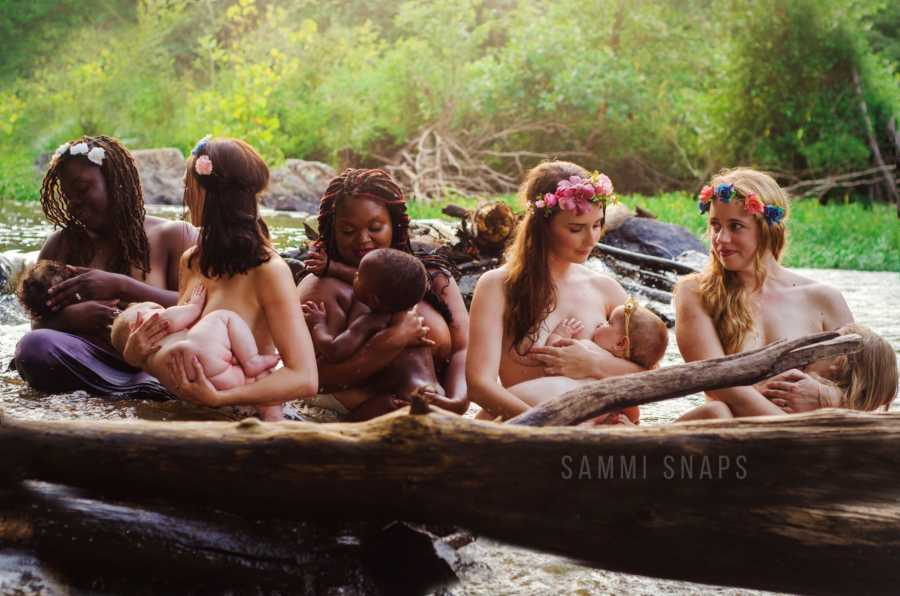 Group of mothers wearing flower crowns sit in river breastfeeding