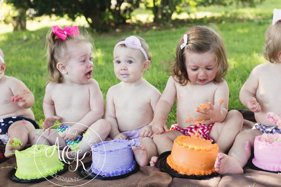 Shirtless infants sit in line with colorful cakes in front of them