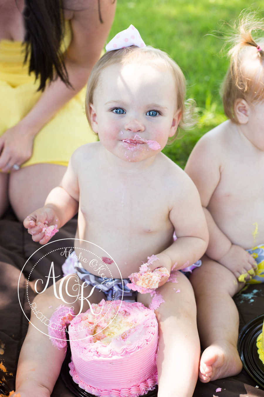 Infant with pink cake in front of her and frosting on her hands and mouth