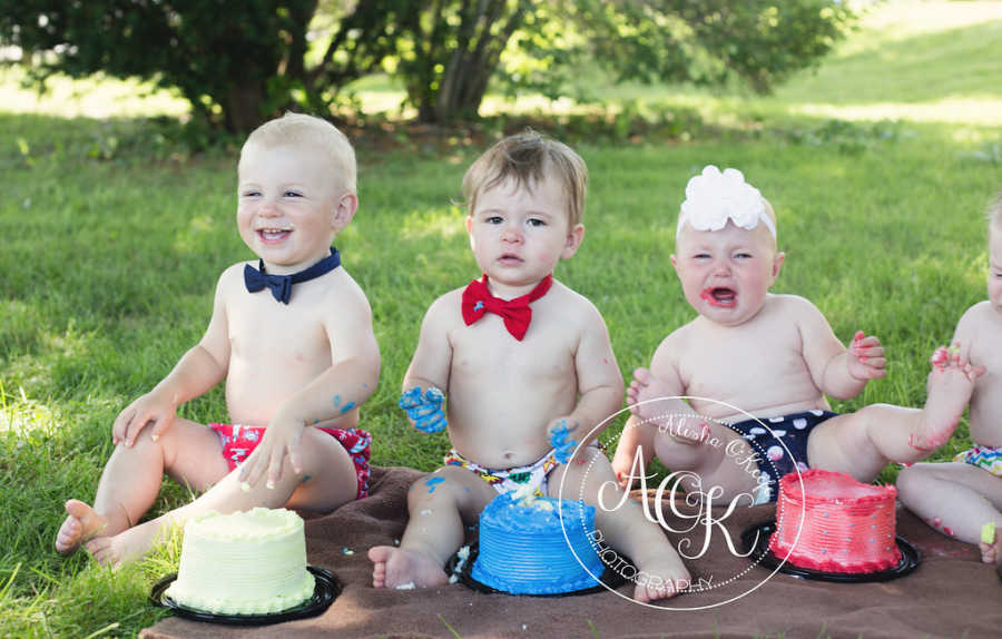 Three shirtless infants sitting with cake in front of them and frosting all over them