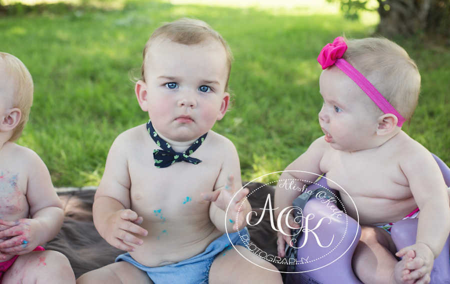 Infants sitting on ground in line with colorful frosting on them