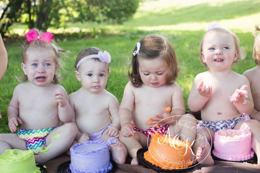 Shirtless toddlers sitting in line with cake in front of them