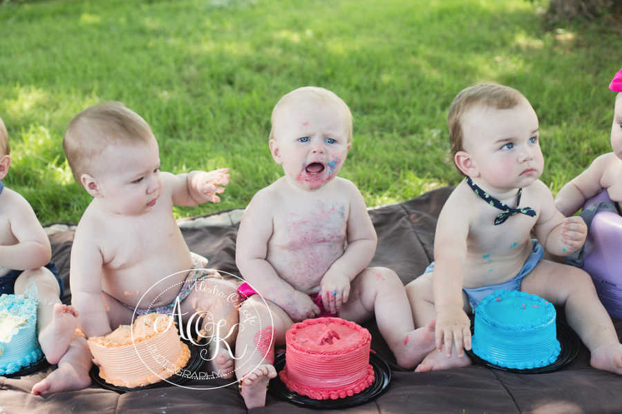 Infants sitting on ground with cake in front of them and frosting on them