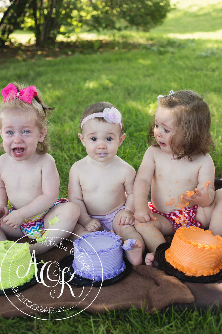 Three infants sit on ground crying with cake in front of them
