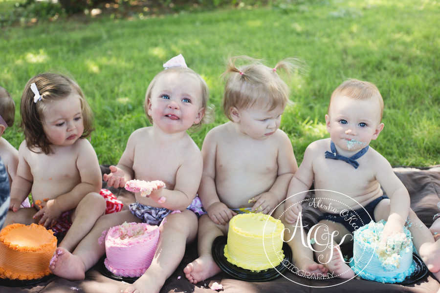 Infants sit on ground with cake in front of them looking at each other