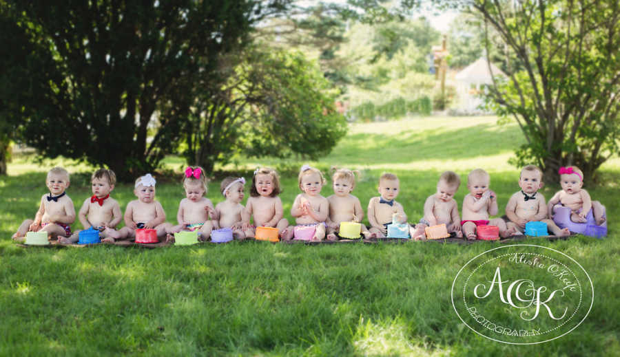 Infants sitting on ground in line with colorful cakes in front of them