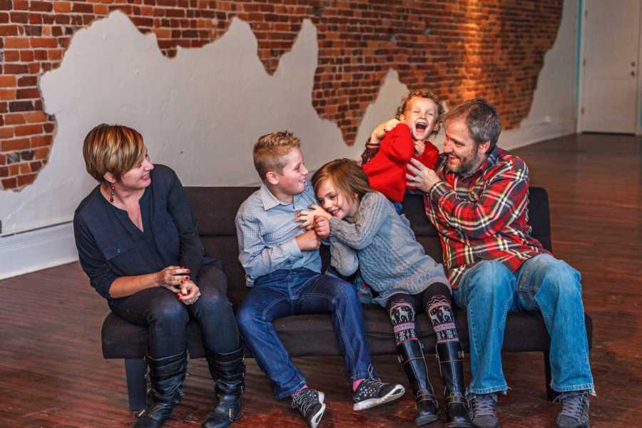 Husband and wife sit on opposite ends of couch with three adopted children in between them