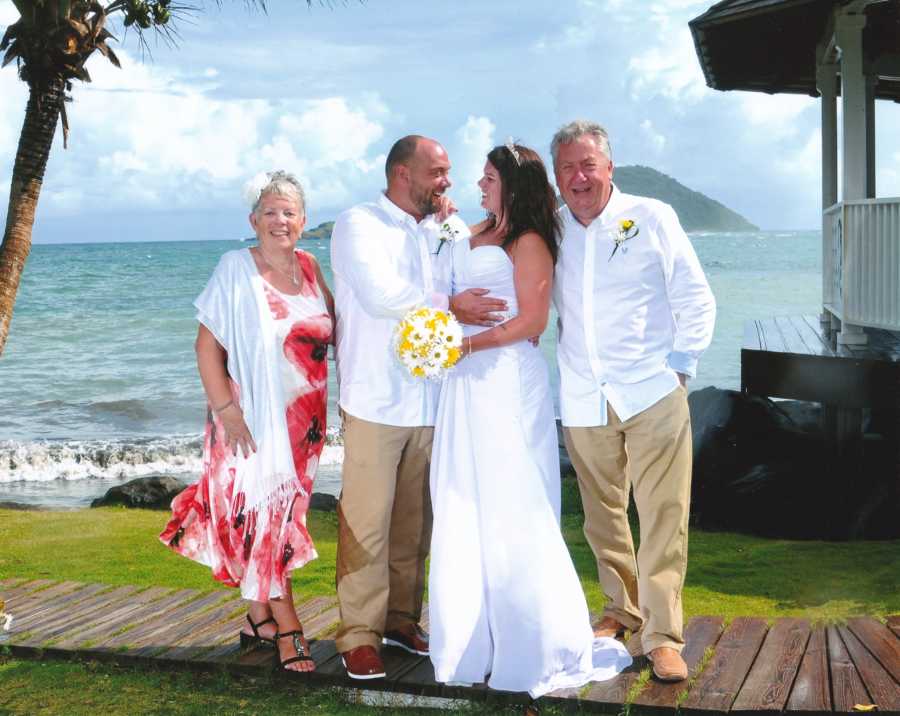 Mother and father stand with adopted daughter and her husband at their wedding on beach front